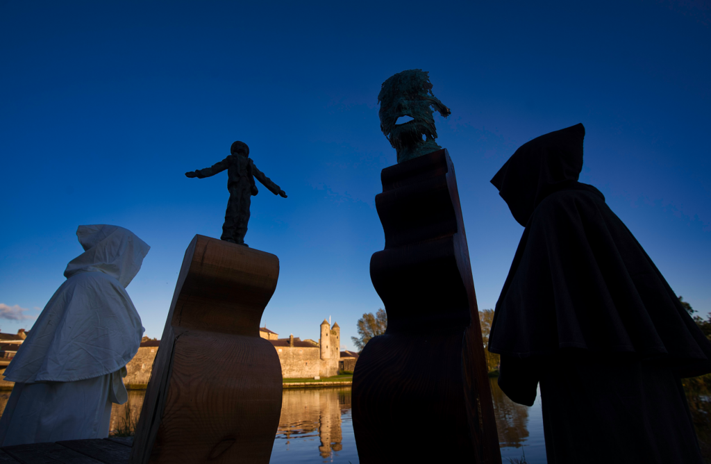 Person in white hood and three large chess pieces against a deep blue sky