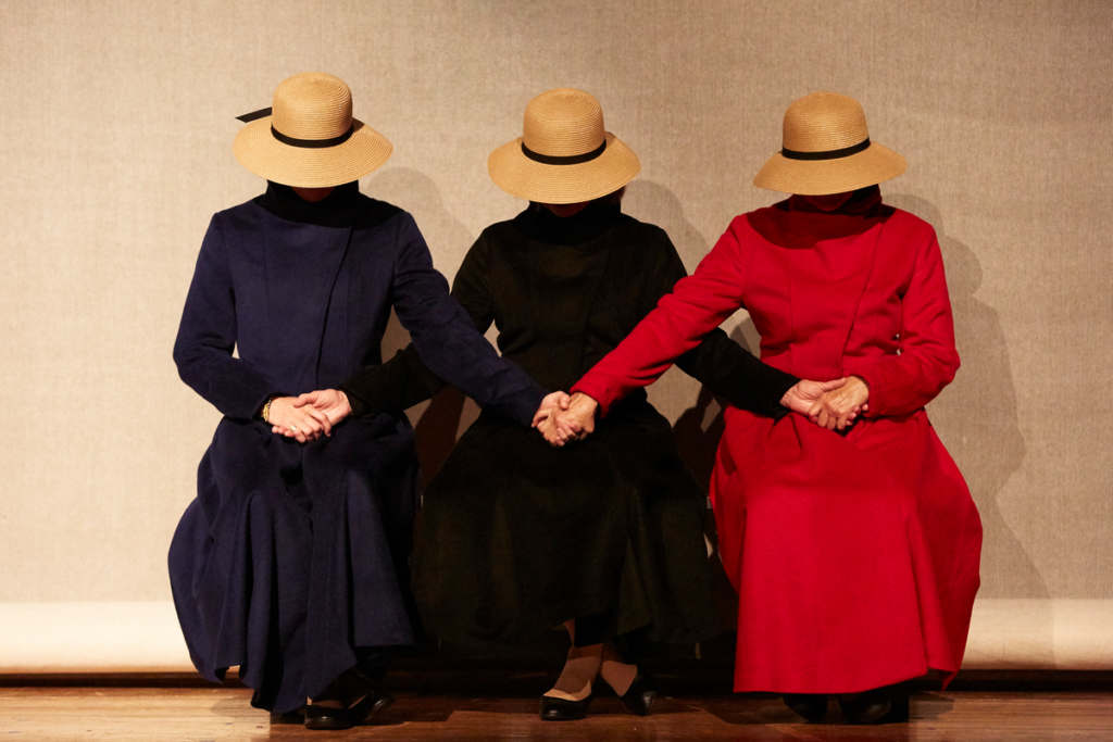 Adult woman reading from a book, audience members are seen in the foreground